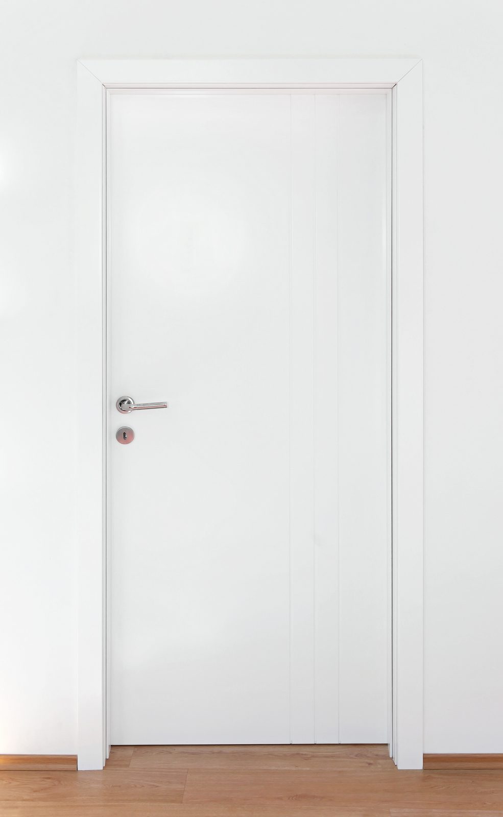 Porta lisa branca da Linha Popular, com maçaneta inox, em parede branca.